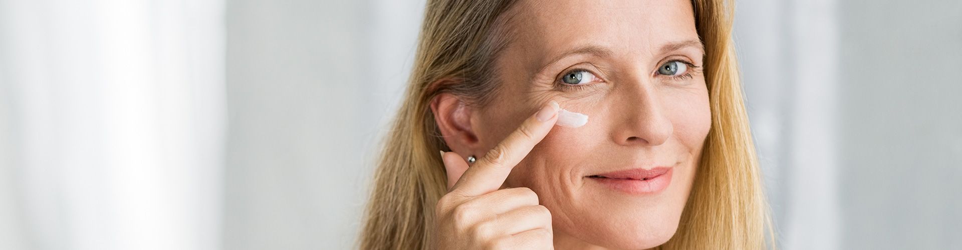 Blonde Frau cremt Gesicht vor dem Spiegel.